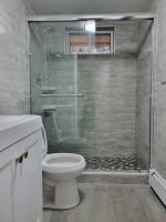 Renovated bathroom with glass shower, modern tile, and laundry facilities in East Orange apartment.