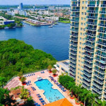 Aerial view of a luxury apartment building with a pool, surrounded by greenery and waterways in Sunny Isles.