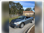 2010 Chrysler Sebring Limited convertible with 141,000 miles parked on the road, surrounded by trees.