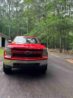 Front view of a red 2015 Chevrolet Silverado 1500 High Country parked on a road in a natural setting.