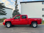 2011 Chevrolet Silverado 1500 LT 4WD pickup truck in red, parked on a road with trees in the background.