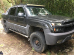 2013 Chevy Avalanche 1500 Z71 4WD parked in a wooded area, showing off its rugged design and powerful tires.