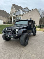 Black Jeep Wrangler Unlimited 4 Door SUV parked in front of a house, featuring heavy upgrades and excellent condition.