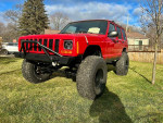 2000 Jeep Cherokee XJ in red with new suspension and upgraded tires parked on grass