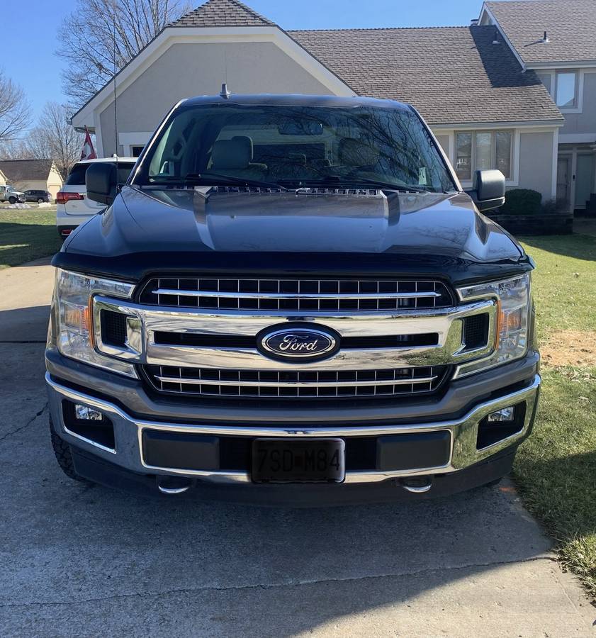 Front view of a 2018 Ford F150 XLT in brown color with shiny grille and robust design, parked at a residential location.
