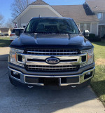 Front view of a 2018 Ford F150 XLT in brown color with shiny grille and robust design, parked at a residential location.