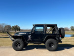 2006 Jeep Wrangler with 4-inch lift and 35-inch tires parked outdoors against a clear blue sky.
