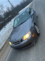 2007 Saab 9.3 with 155,000 miles parked on a snowy road, showcasing its sleek design and headlights.