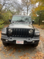 Front view of a 2023 Jeep Wrangler Sport 4WD in grey with hard-top, showcasing its design and features.