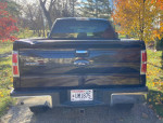 Rear view of a 2013 Ford F150 XLT, black, with a solid frame and 127,600 miles, parked outdoors.