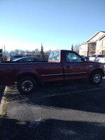 Red Ford F250 pickup truck with clean body, needs engine repair, parked in a lot under clear blue sky.