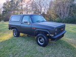 1987 GMC Jimmy Sierra Classic in satin black with new tires, parked on grass under sunlight.