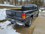 Rear view of a 2005 GMC Sierra 2500 SLT with rust on bumpers, parked on a snowy driveway.