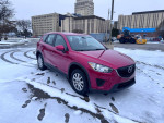 2014 Mazda CX-5 Sport in red, parked on snowy ground with buildings in the background.