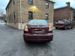 Rear view of a 2008 Suzuki SX4 sedan parked in a driveway, showcasing its reliable design and new tires.