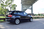 2013 BMW X5 xDrive35i AWD parked under a bridge with lush trees in the background, showcasing its sleek design.