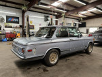 1972 BMW 2002 Tii project car in a workshop, features tan Recaro seats and disassembled engine components.