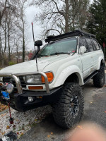 Toyota Landcruiser with off-road modifications, including lift kit and winch, parked amidst trees.
