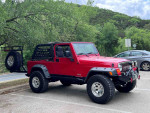 2005 Jeep LJ Unlimited in red parked near greenery, showcasing its pristine condition and off-road capabilities.