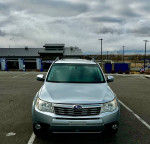 Front view of a 2013 Subaru Forester parked, featuring a silver exterior and cloudy sky background.