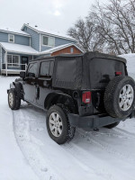 2014 Jeep Wrangler Sahara 4WD parked in snowy driveway, showcasing its exterior and off-road tires