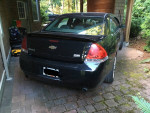 Rear view of a 2007 black Chevrolet Impala SS parked in a driveway surrounded by foliage.