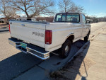 Rear view of a clean 1992 Ford F-150 with a long bed and new tires parked on the street.
