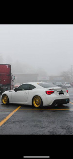 2015 Subaru BRZ with gold wheels and aftermarket modifications, parked in a foggy lot.