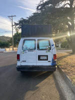 Rear view of a 2003 Adventure van with stickers parked on the street, spacious interior, and ready for travel.