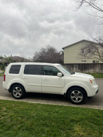 Side view of a white 2014 Honda Pilot EX FWD parked with cloudy sky and green grass.