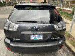 Rear view of a 2008 Lexus RX400h hybrid with rain on the windshield, parked on a city street.