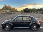 Side view of a black 2016 Volkswagen Beetle coupe parked in a lot during sunset.