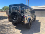 1994 Land Rover Defender 110 with upgraded features and new tires, parked in a sunny setting.