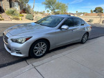 2014 Infiniti Q50 Premium sedan in silver color parked on the street with clear sky and desert landscape.