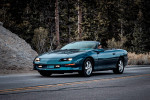 1997 Chevrolet Camaro Z28 convertible driving on a scenic road with trees in the background