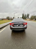 Rear view of a grey 2020 Honda Accord Sport FWD parked on a wet road, showcasing modern design.