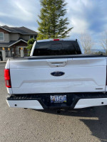 Rear view of a 2018 Ford F150 Lariat in white with a black tonneau cover in a residential area.