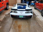 Rear view of a white 2014 Chevrolet Corvette parked in a driveway with various vehicles nearby.