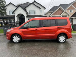Side view of a 2022 Ford Transit Connect passenger wagon in red with 66,000 miles parked on a residential street.