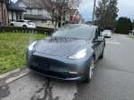 2023 Tesla Model Y in gray parked on the street, featuring modern design and sleek headlights.