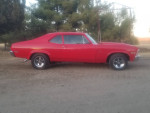 1972 Chevrolet Nova in bright red, parked on gravel with clean interior and custom wheels.
