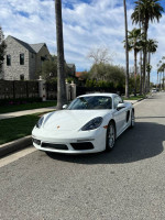 2018 Porsche 718 Cayman in pristine condition parked on a street, showcasing its sleek white design and clean lines.