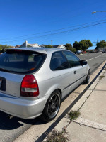 2000 Honda Civic hatchback in silver with black wheels parked on the street, showcasing its sporty design and condition.
